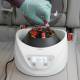 Globe Scientific GCC-P Portable Clinical Centrifuge - A Gloved hand placing a Test Tube with red liquid into the right side of a centrifuge inside a car (Test tubes are sold separately)